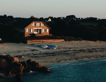 wide-shot-brown-house-sandy-seashore-by-sea-surrounded-with-rocks-trees